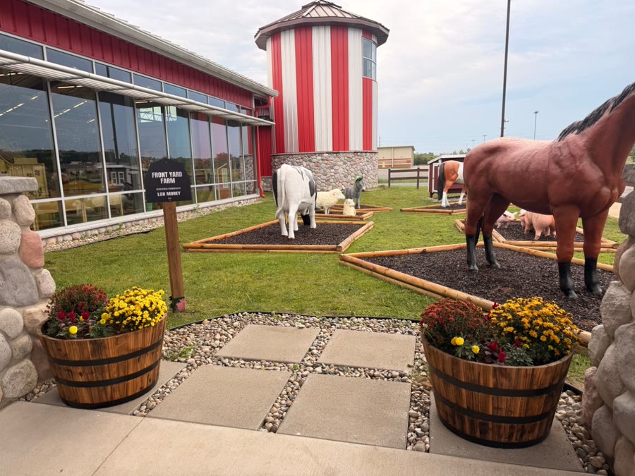 The Front Yard Farm entrance with its welcome sign, barrel planters full of mums, and the museum's red silo behind