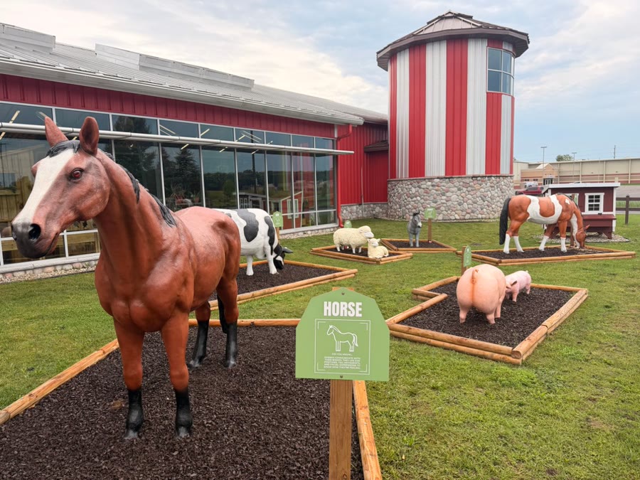 A life-size horse standing in its garden bed beside the HORSE sign, with pigs, sheep, and a cow in the beds behind
